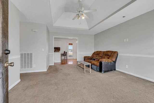 living area with ceiling fan, a raised ceiling, and light carpet