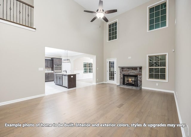 unfurnished living room featuring light wood-type flooring, ceiling fan, sink, a high ceiling, and a stone fireplace