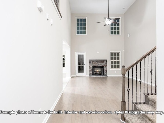 unfurnished living room featuring a stone fireplace, ceiling fan, wood-type flooring, and a high ceiling