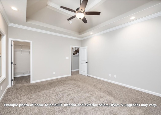 unfurnished bedroom featuring carpet flooring, ceiling fan, a walk in closet, and a tray ceiling