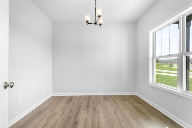 spare room with a notable chandelier, a wealth of natural light, and light hardwood / wood-style flooring