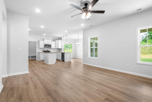 unfurnished living room featuring ceiling fan with notable chandelier, light wood-type flooring, and sink