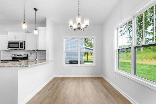 kitchen with stainless steel appliances, light stone counters, backsplash, decorative light fixtures, and white cabinets