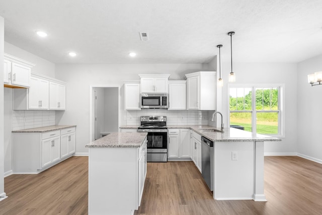 kitchen with stainless steel appliances, sink, decorative light fixtures, a center island, and white cabinetry