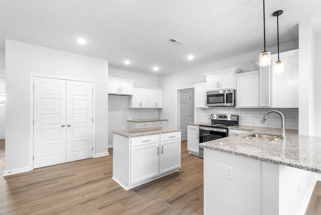 kitchen featuring sink, stainless steel appliances, a kitchen island, pendant lighting, and white cabinets