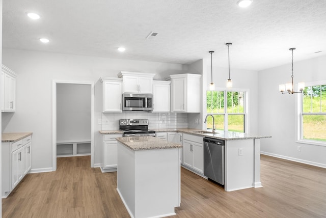 kitchen featuring white cabinets, decorative light fixtures, a center island, and stainless steel appliances