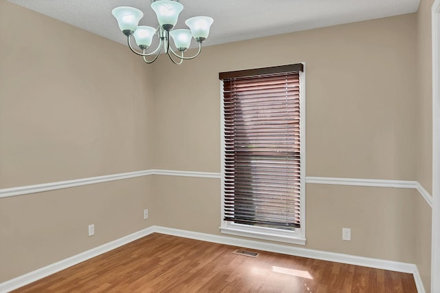 spare room featuring hardwood / wood-style flooring and an inviting chandelier