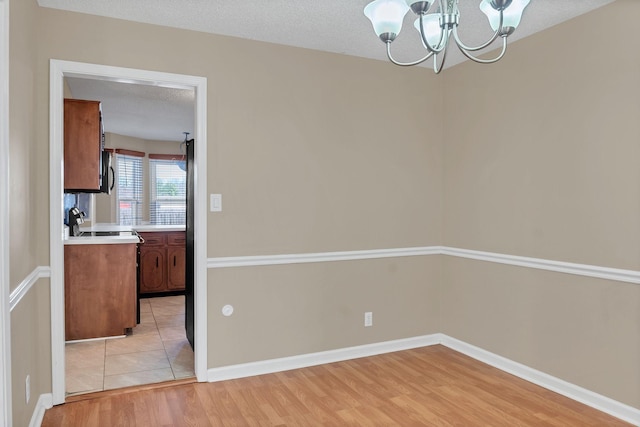 unfurnished dining area with a chandelier, a textured ceiling, and light hardwood / wood-style floors