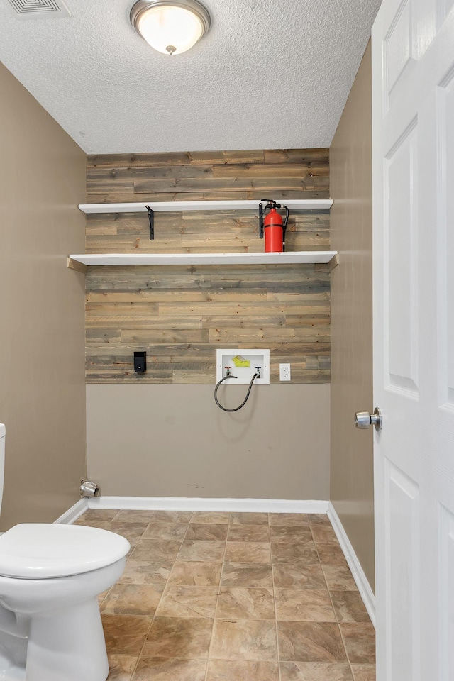 bathroom with a textured ceiling, toilet, and wood walls