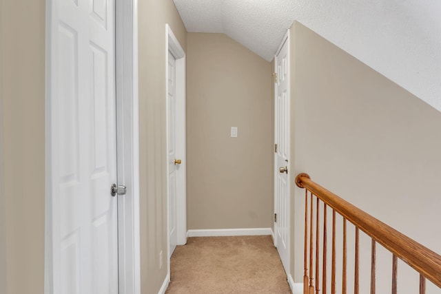 hallway featuring light colored carpet, lofted ceiling, and a textured ceiling