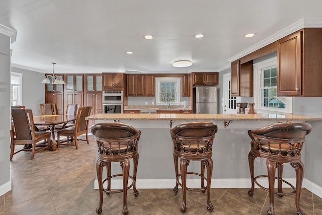 kitchen with hanging light fixtures, light stone counters, a breakfast bar area, appliances with stainless steel finishes, and ornamental molding