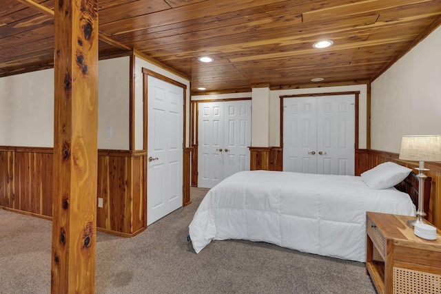 carpeted bedroom featuring wood walls, wooden ceiling, and multiple closets