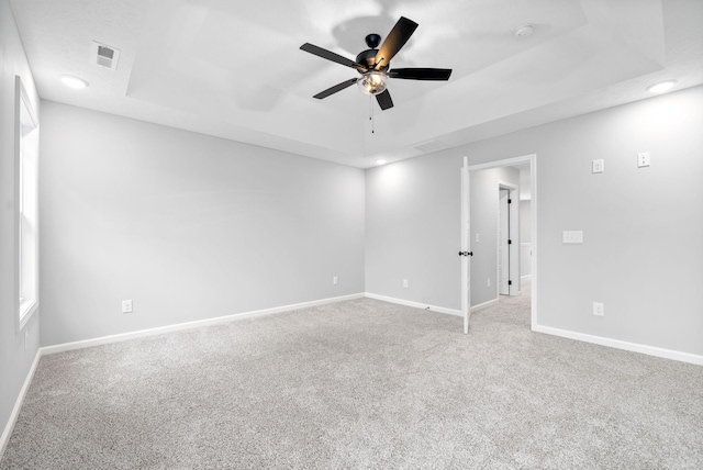 carpeted spare room with a tray ceiling and ceiling fan