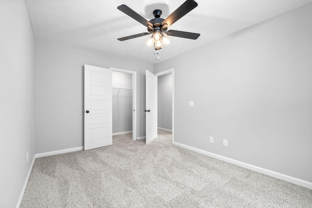 unfurnished bedroom with a walk in closet, ceiling fan, a closet, and light carpet