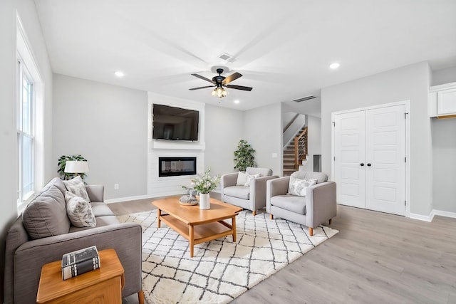 living room featuring ceiling fan, a fireplace, and light hardwood / wood-style flooring