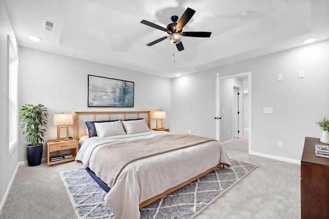 carpeted bedroom with ceiling fan and a raised ceiling