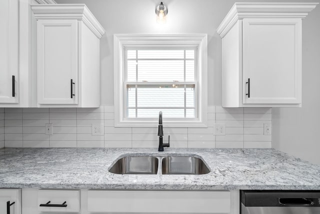 kitchen featuring light stone countertops, backsplash, sink, dishwasher, and white cabinetry