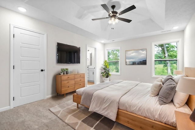 bedroom featuring a tray ceiling, ensuite bath, ceiling fan, and carpet floors