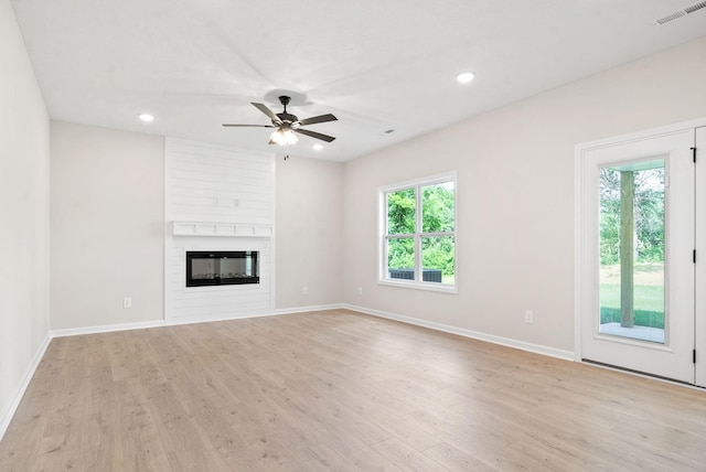 unfurnished living room featuring a healthy amount of sunlight, a large fireplace, ceiling fan, and light hardwood / wood-style floors