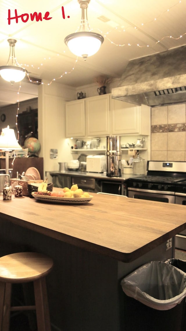 kitchen featuring gas stove, extractor fan, pendant lighting, butcher block countertops, and white cabinetry