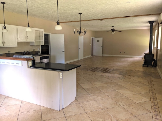 kitchen featuring a wood stove, ceiling fan with notable chandelier, stainless steel dishwasher, decorative light fixtures, and white cabinetry