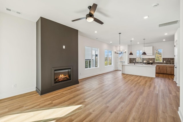 unfurnished living room featuring ceiling fan with notable chandelier and light wood-type flooring