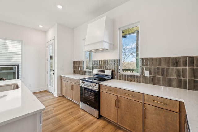 kitchen with tasteful backsplash, light hardwood / wood-style flooring, stainless steel range oven, and custom exhaust hood