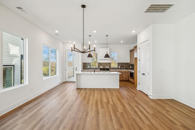 kitchen featuring pendant lighting, an inviting chandelier, sink, light wood-type flooring, and an island with sink