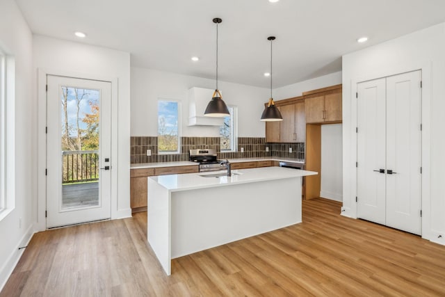 kitchen with decorative backsplash, a kitchen island with sink, sink, stainless steel range oven, and hanging light fixtures