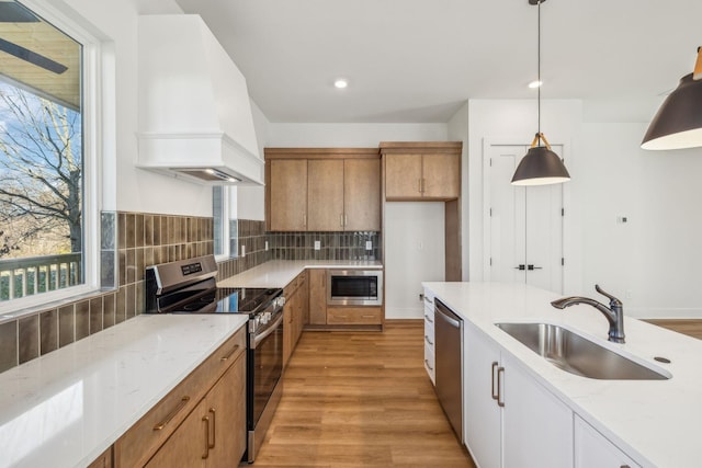 kitchen with appliances with stainless steel finishes, backsplash, custom exhaust hood, sink, and pendant lighting