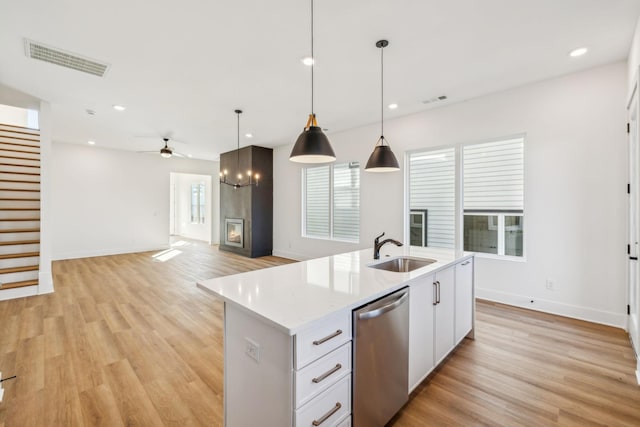 kitchen featuring a kitchen island with sink, sink, hanging light fixtures, stainless steel dishwasher, and white cabinetry