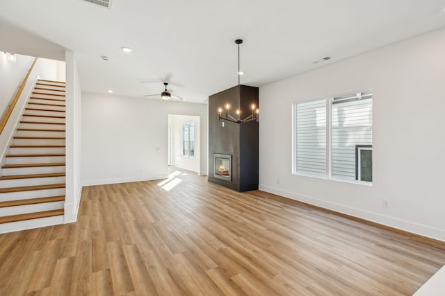 unfurnished living room with a large fireplace, light hardwood / wood-style floors, and ceiling fan with notable chandelier