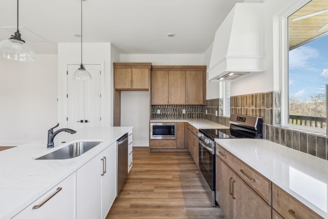 kitchen with custom exhaust hood, sink, decorative light fixtures, white cabinetry, and stainless steel appliances