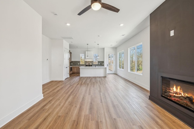 unfurnished living room featuring ceiling fan, a fireplace, and light hardwood / wood-style flooring