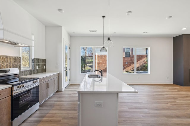 kitchen with stainless steel range, hanging light fixtures, tasteful backsplash, light hardwood / wood-style floors, and a center island with sink