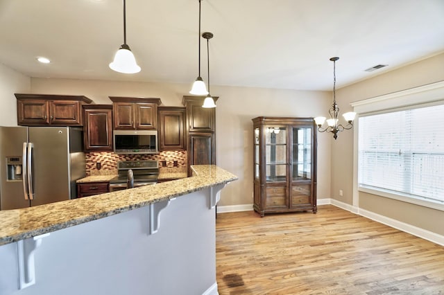 kitchen featuring decorative backsplash, appliances with stainless steel finishes, light stone counters, a breakfast bar, and hanging light fixtures