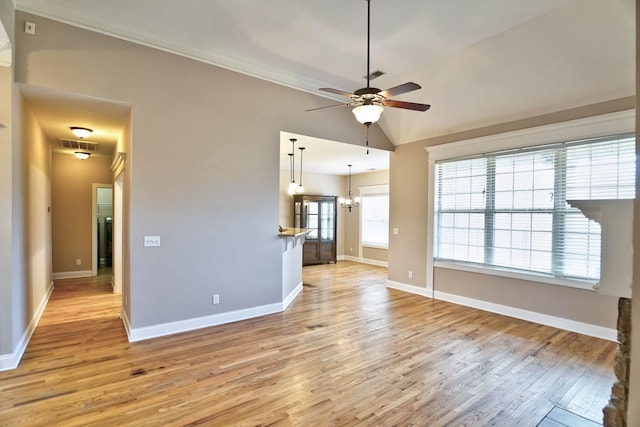 unfurnished living room with ceiling fan with notable chandelier, light wood-type flooring, and vaulted ceiling