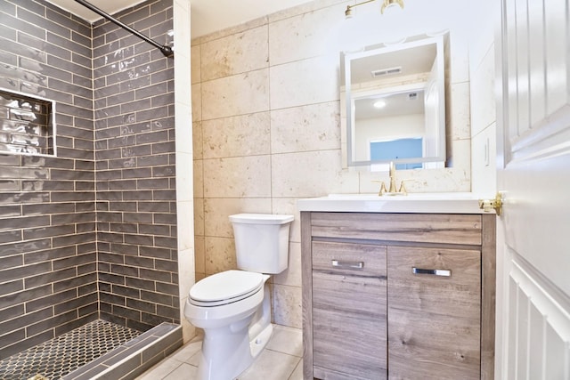 bathroom with tile patterned flooring, tiled shower, toilet, vanity, and tile walls