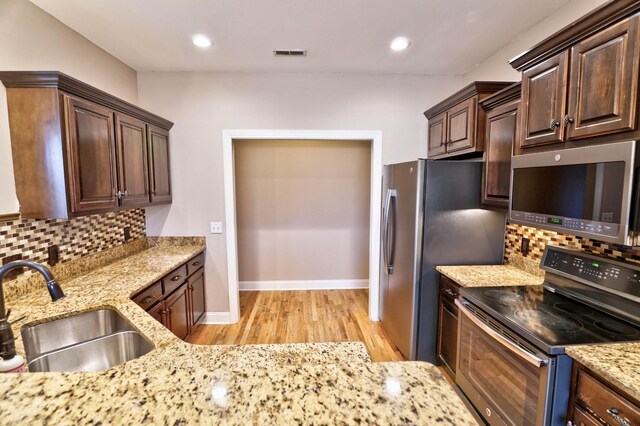 kitchen featuring decorative backsplash, light stone countertops, sink, and appliances with stainless steel finishes