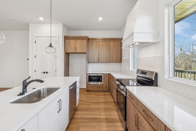 kitchen with white cabinetry, sink, hanging light fixtures, appliances with stainless steel finishes, and custom exhaust hood