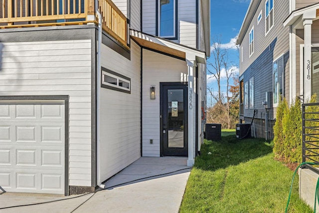 property entrance featuring a balcony, a garage, cooling unit, and a lawn