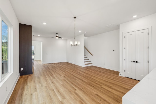 unfurnished living room featuring ceiling fan with notable chandelier and light wood-type flooring