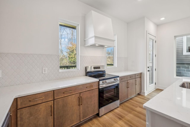 kitchen featuring backsplash, premium range hood, appliances with stainless steel finishes, light hardwood / wood-style floors, and light stone counters