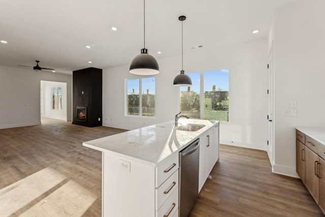 kitchen with light stone countertops, stainless steel dishwasher, ceiling fan, a center island with sink, and white cabinets