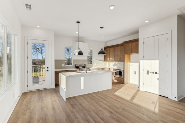 kitchen with stainless steel appliances, sink, decorative light fixtures, light hardwood / wood-style floors, and an island with sink