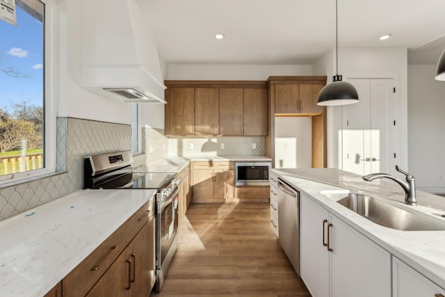 kitchen featuring appliances with stainless steel finishes, custom range hood, sink, pendant lighting, and white cabinets