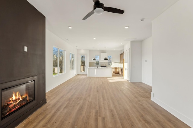 unfurnished living room featuring ceiling fan, a large fireplace, and light hardwood / wood-style flooring