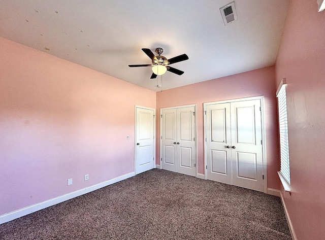 unfurnished bedroom featuring ceiling fan, dark carpet, and multiple closets