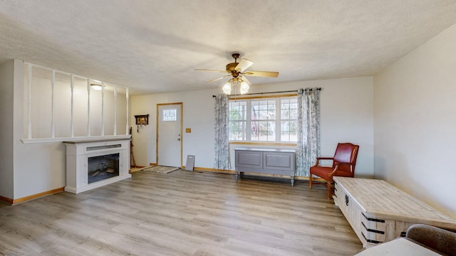 sitting room with ceiling fan, a fireplace, a textured ceiling, and light wood-type flooring