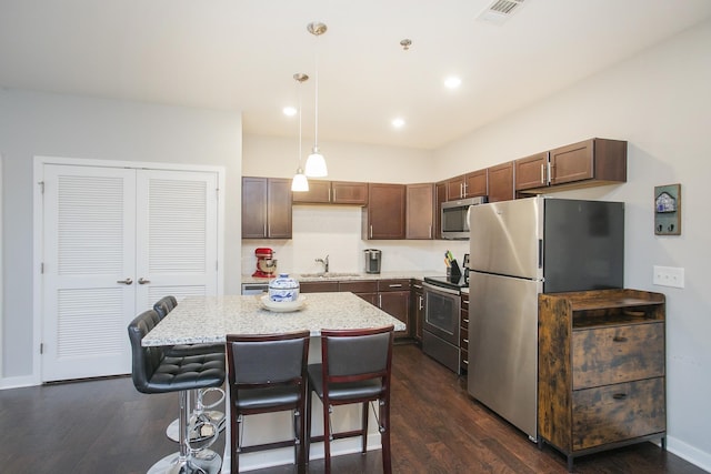 kitchen featuring stainless steel appliances, dark wood-type flooring, sink, decorative light fixtures, and a center island